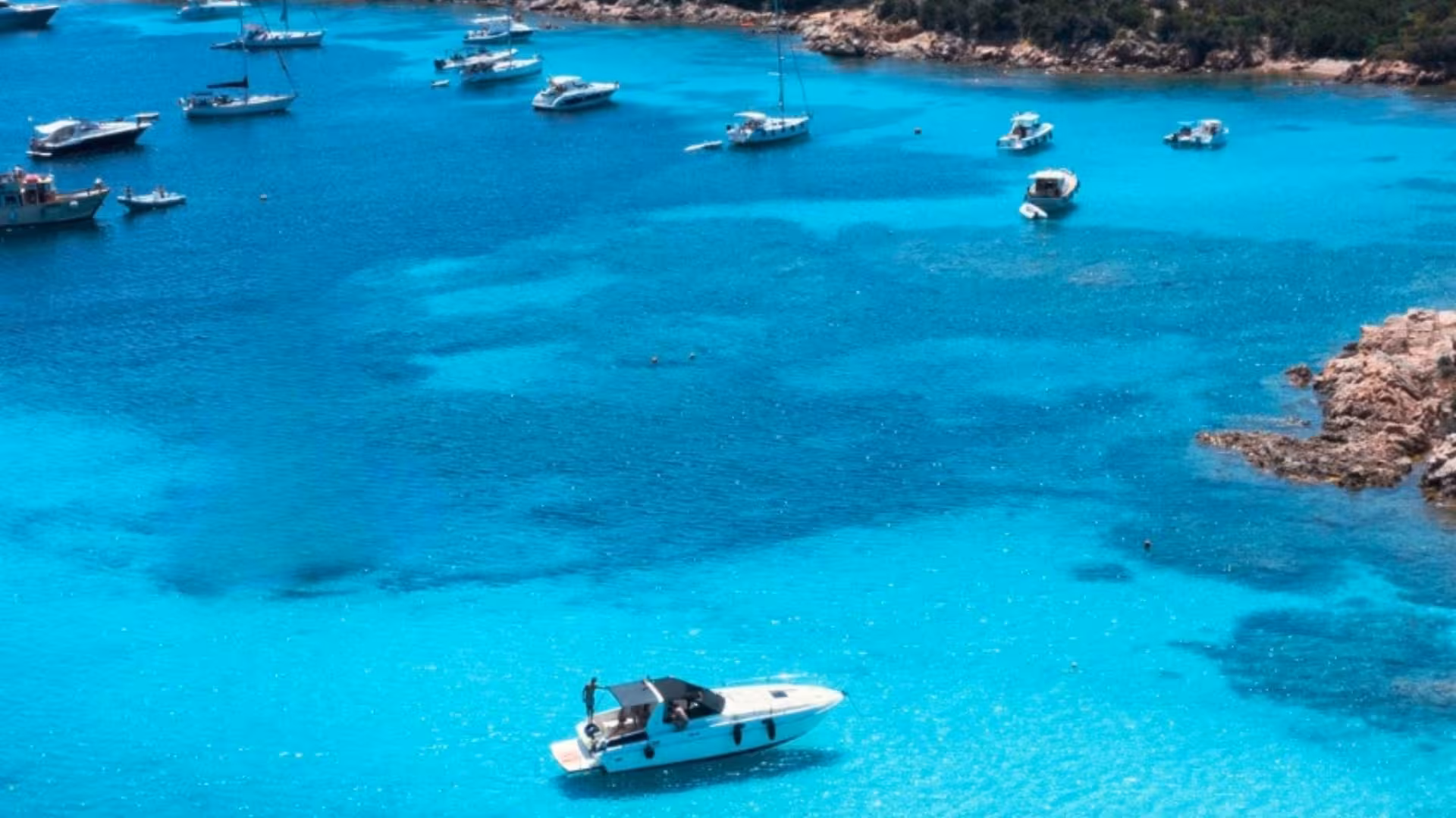 Scenic view of boats floating in the turquoise waters of La Maddalena Archipelago on a sunny day.