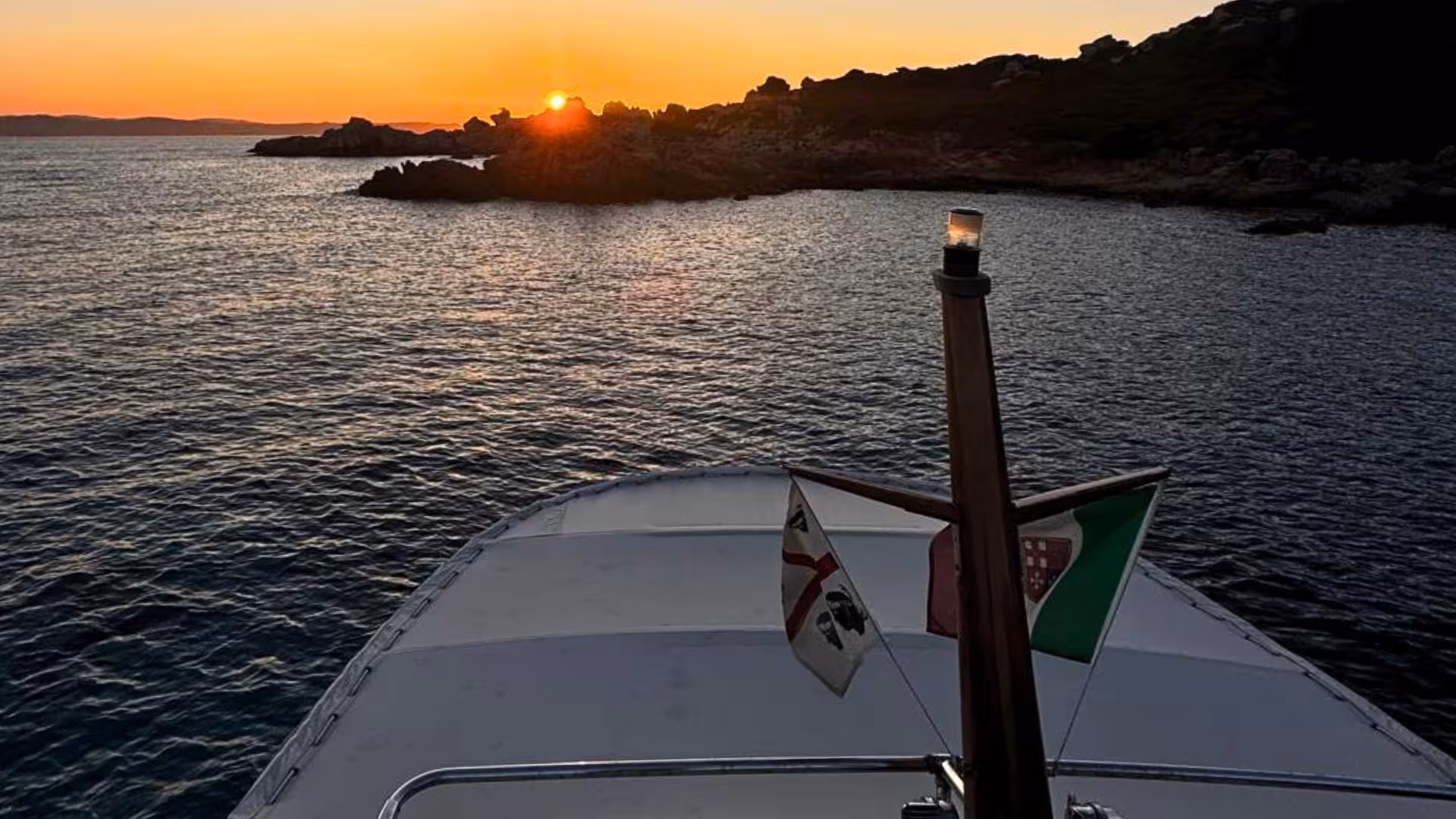 Experience a breathtaking sunset over rocky shores from a boat in La Maddalena Archipelago.
