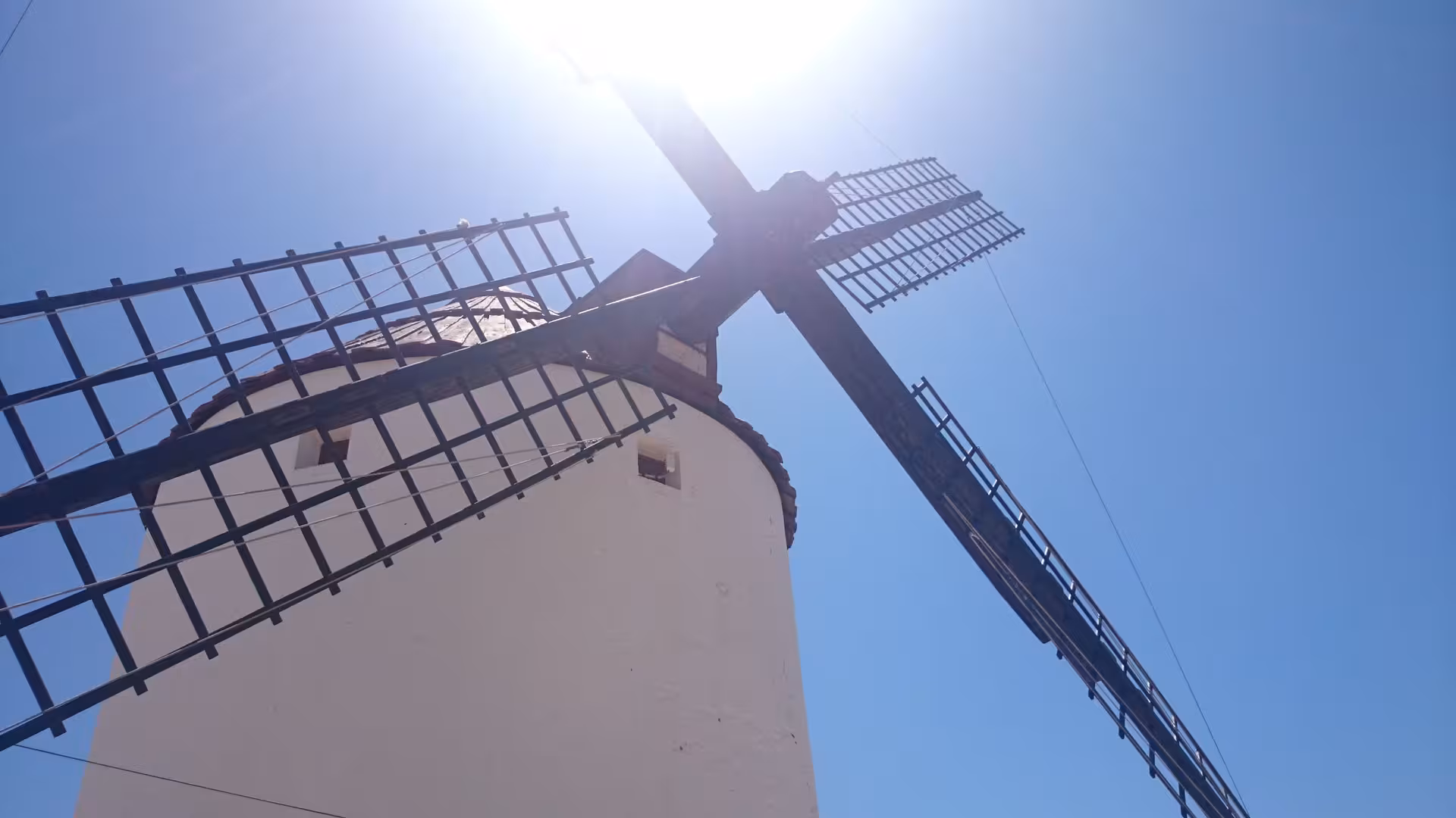 Low-angle view of La Mancha windmill blades against blue sky, iconic landmark on the Don Quixote tour Spain