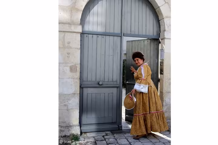 Guide in 18th century golden merchant dress standing by historic stone archway in La Rochelle