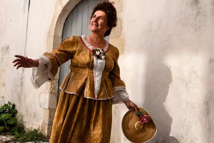 Woman in 18th century golden merchant dress holding a hat in La Rochelle