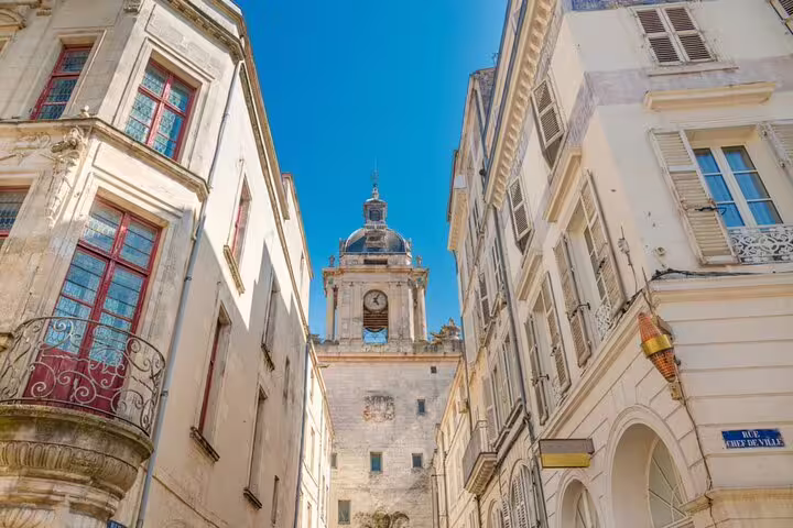 Narrow street in La Rochelle Old Town with historic clock tower and classic French architecture under blue sky
