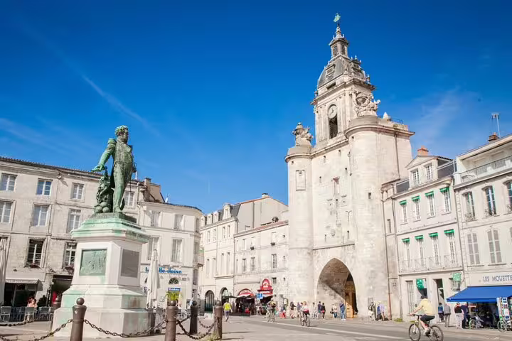 Historic clock tower gate and bronze statue in La Rochelle Old Town square on a sunny day