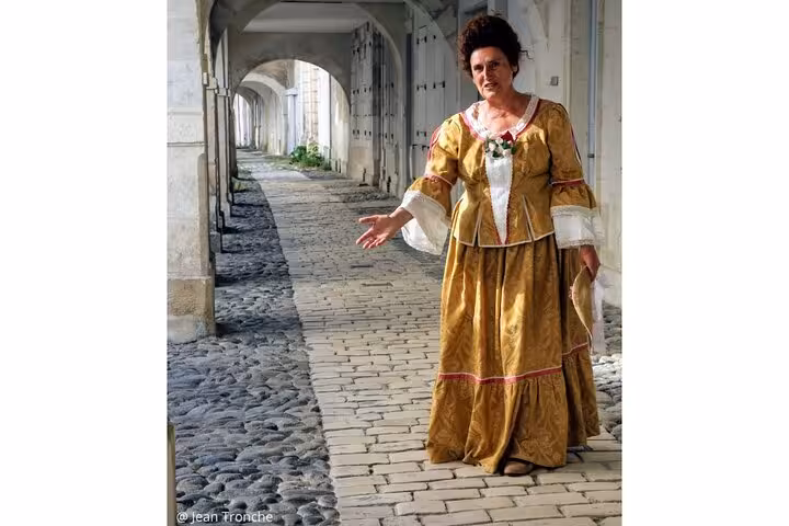 Guide in ornate golden 18th century gown standing on cobblestone arcade in La Rochelle