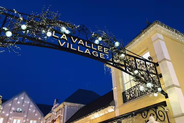 La Vallée Village entrance arch with festive lights at dusk, luxury outlet shopping near Paris