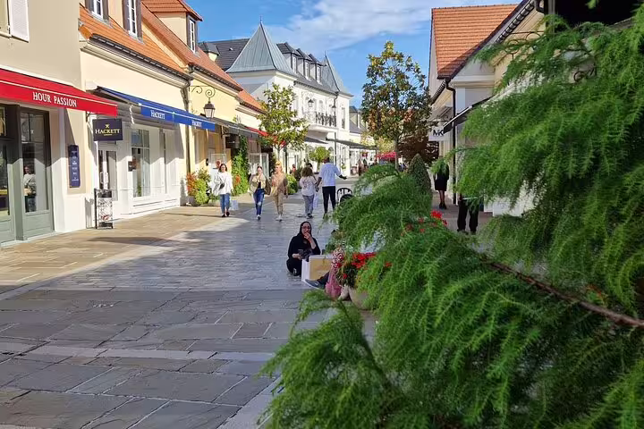 Shoppers strolling La Vallée Village luxury outlet promenade, perfect stop on round-trip Paris private transfer for 1-3