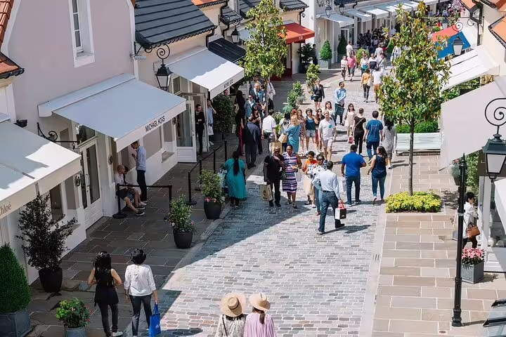 Shoppers strolling cobblestone promenade at La Vallée Village luxury outlet with boutique storefronts