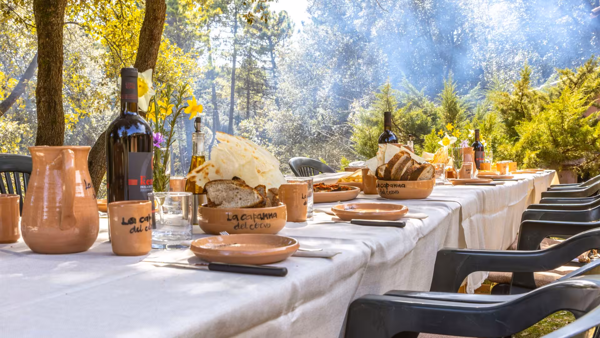 Rustic outdoor dining setup with local delicacies and wine amidst the tranquil Laconi forest backdrop.