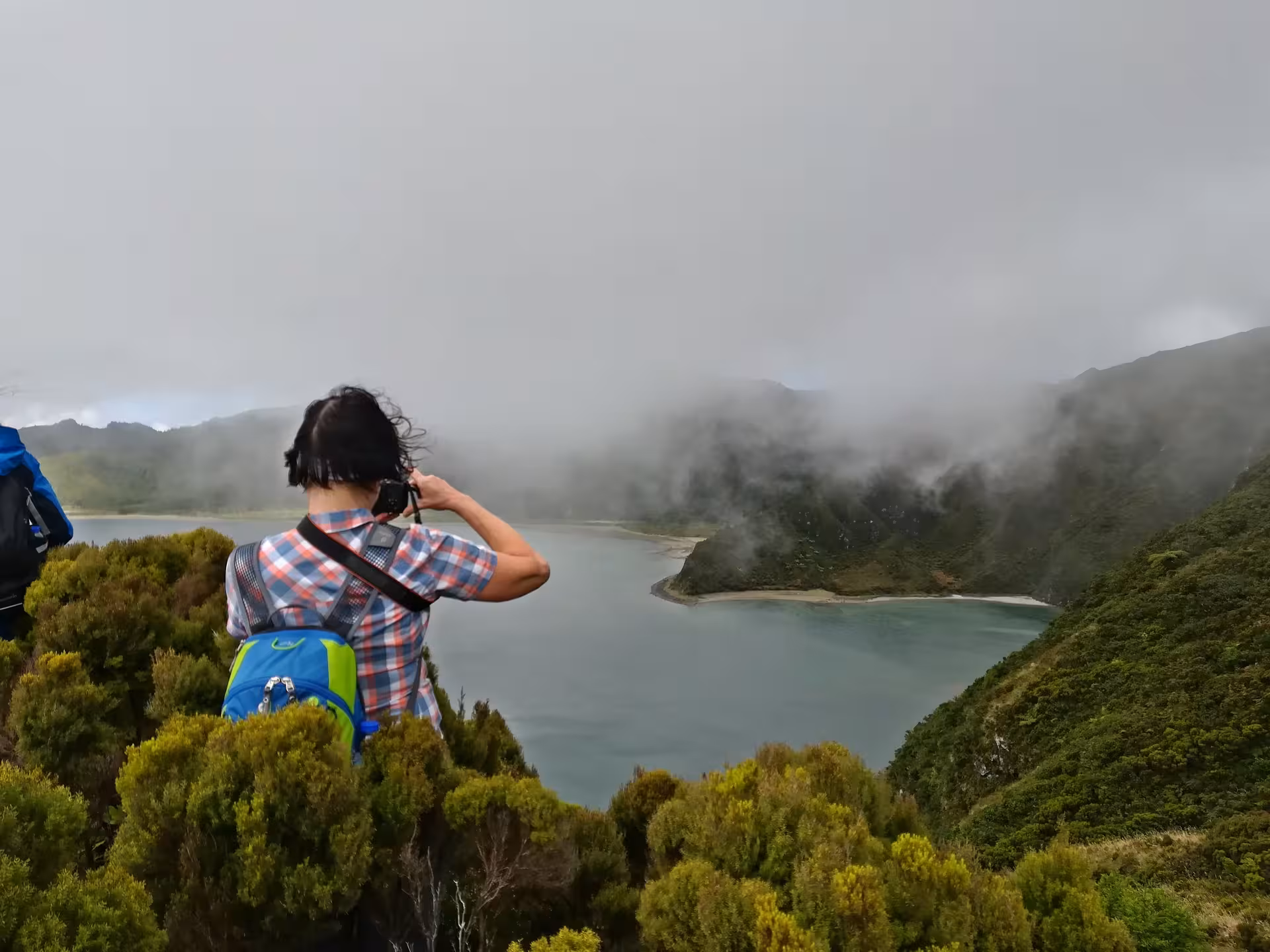Hiker photographing misty Lagoa do Fogo crater lake viewpoint on full-day walking tour, Azores