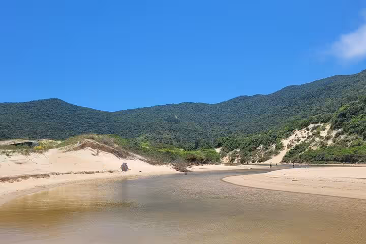 Scenic view of Lagoinha do Leste with sandy beaches and lush green hills under a vibrant blue sky.