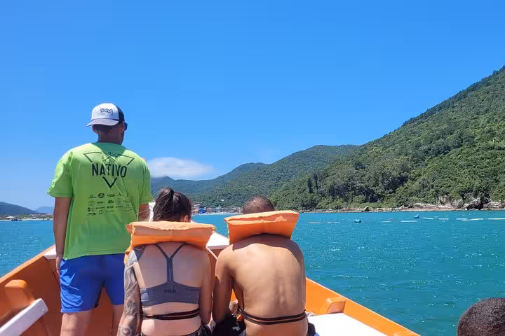 Tourists on a boat explore the turquoise waters near Lagoinha do Leste with lush green hills in the backdrop.