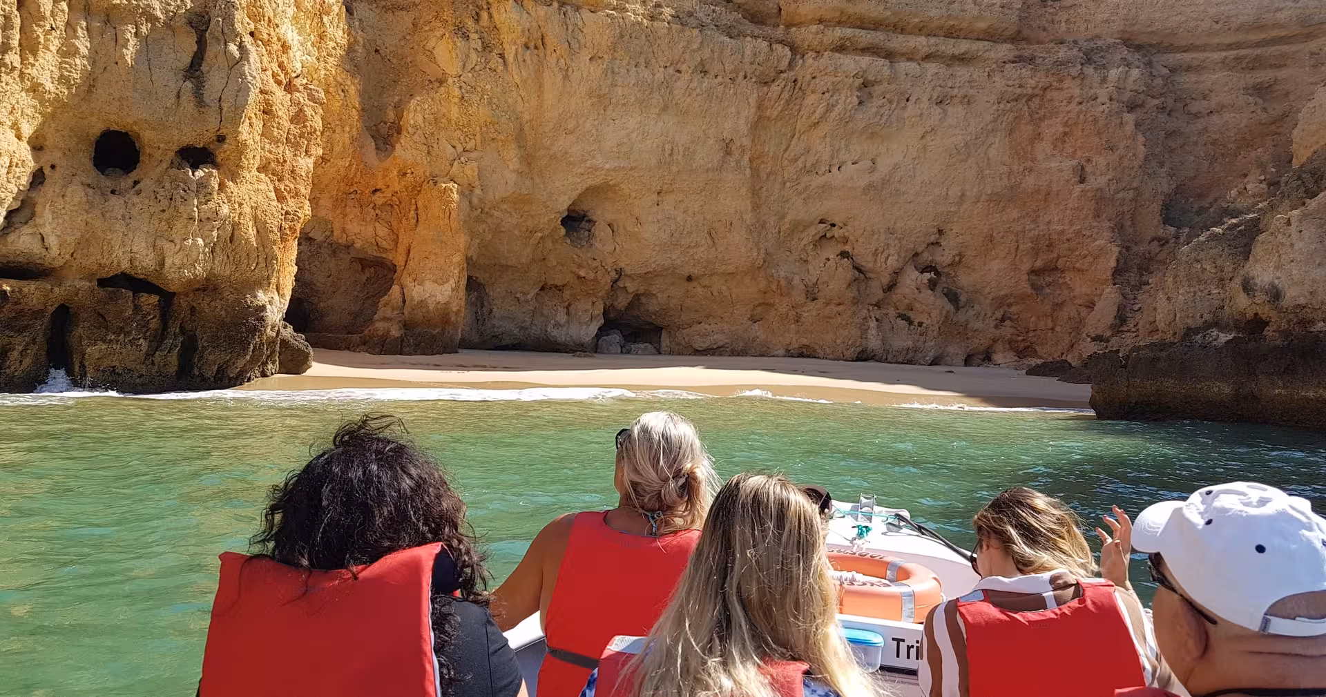 Tourists on a Lagos boat trip approach a hidden sandy beach framed by turquoise water and towering Ponta da Piedade cliffs