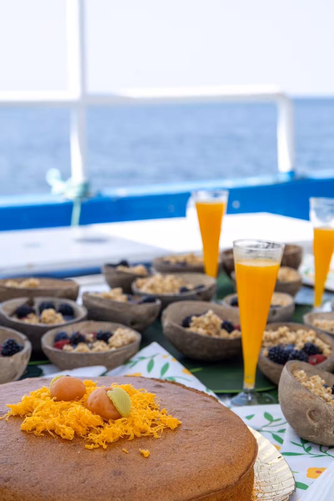 Scenic Lagos brunch cruise spread featuring fresh cake, berry granola bowls, and orange juice with ocean views