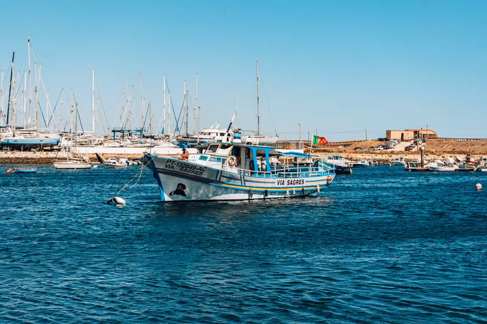 Traditional blue and white boat anchored at Lagos marina ready for scenic coastal caves and cliffs swimming cruise