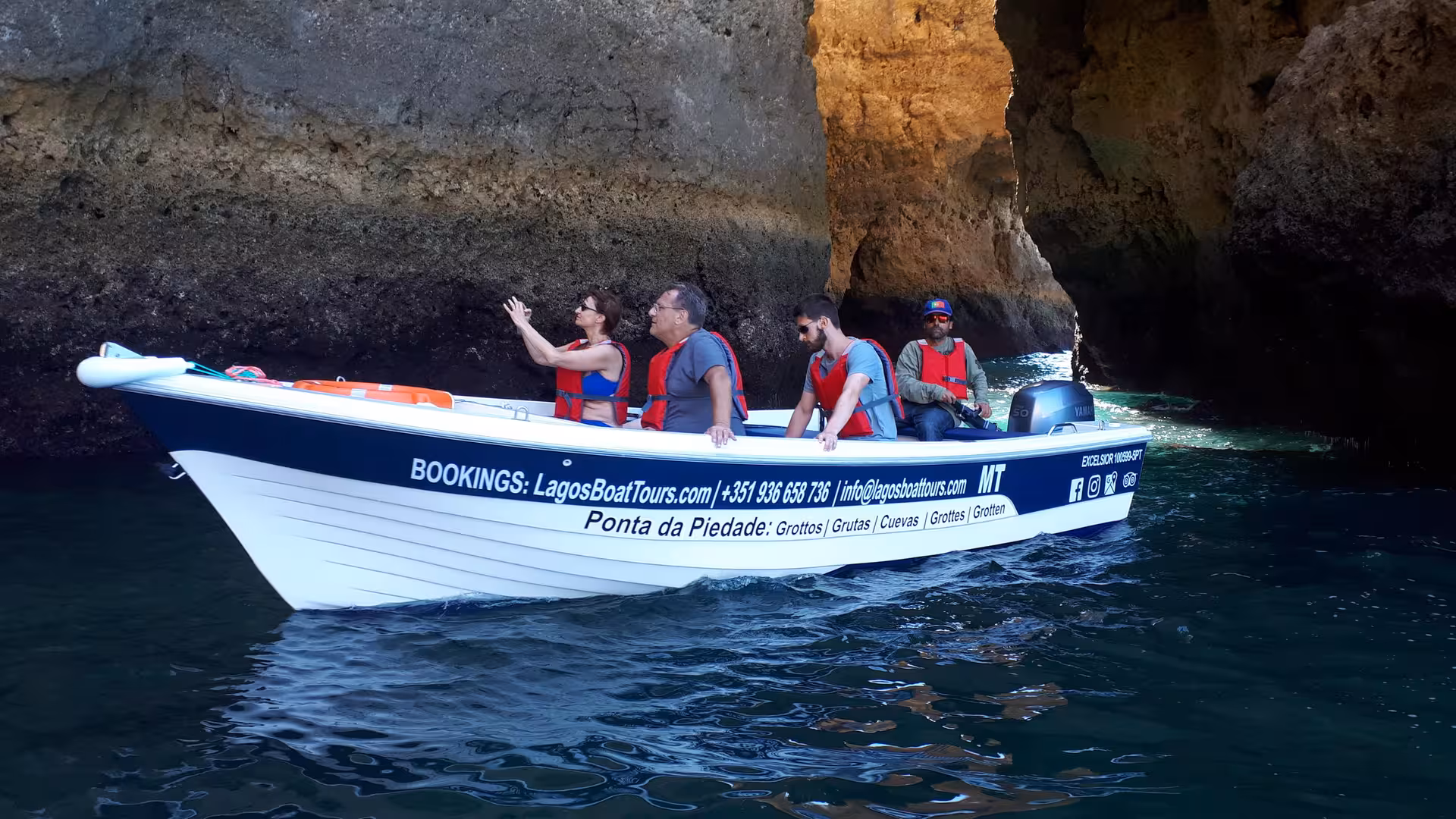 Small Lagos boat tour with guide and passengers in life jackets cruising past towering Ponta da Piedade grotto cliffs