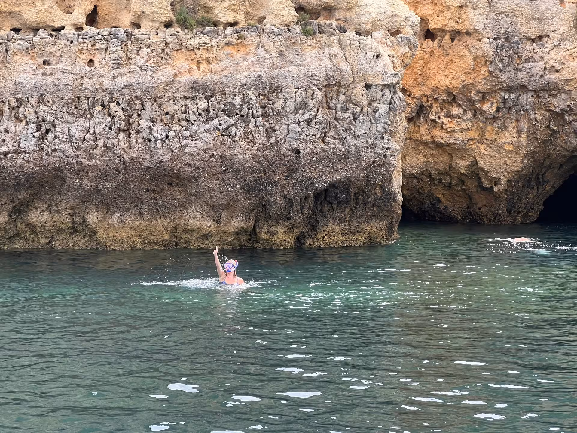 Snorkeler giving thumbs up while swimming near dramatic golden limestone sea caves on Lagos Algarve boat tour