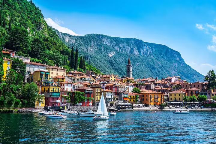 Scenic view of colorful lakeside village and sailboats on Lake Como under a clear blue sky.
