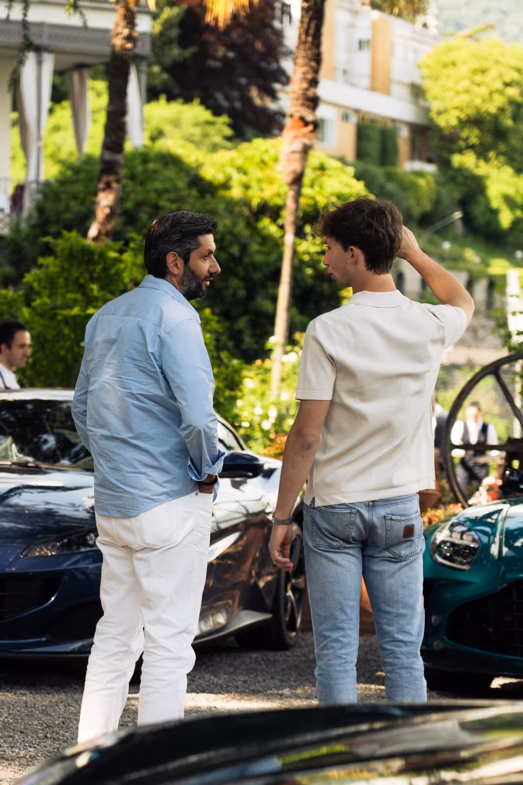 Two guests chat beside luxury supercars at a stunning Lake Como supercar tour meetup in Italy.