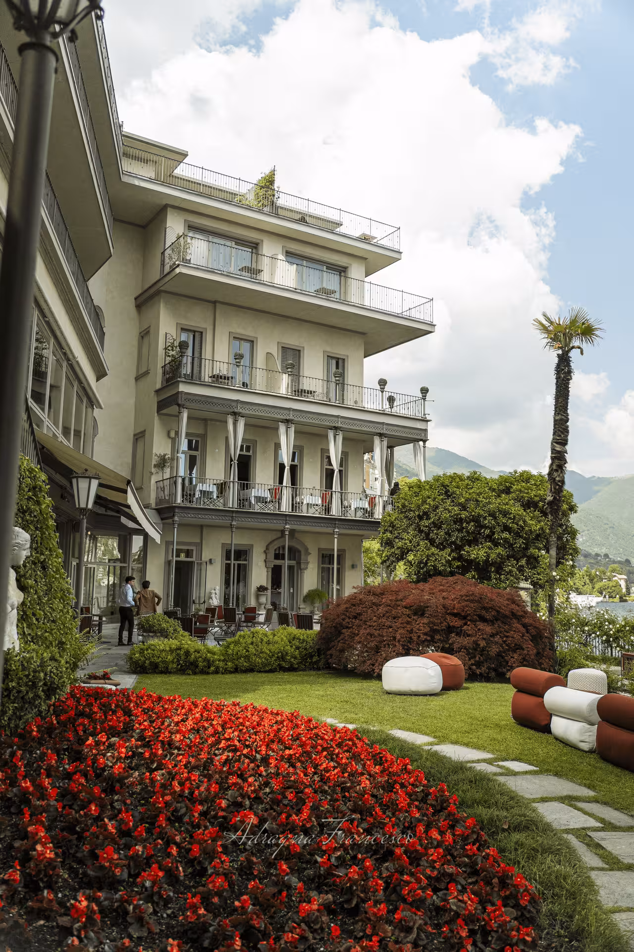 Elegant Lake Como villa with manicured gardens, red flowers, and scenic mountain backdrop
