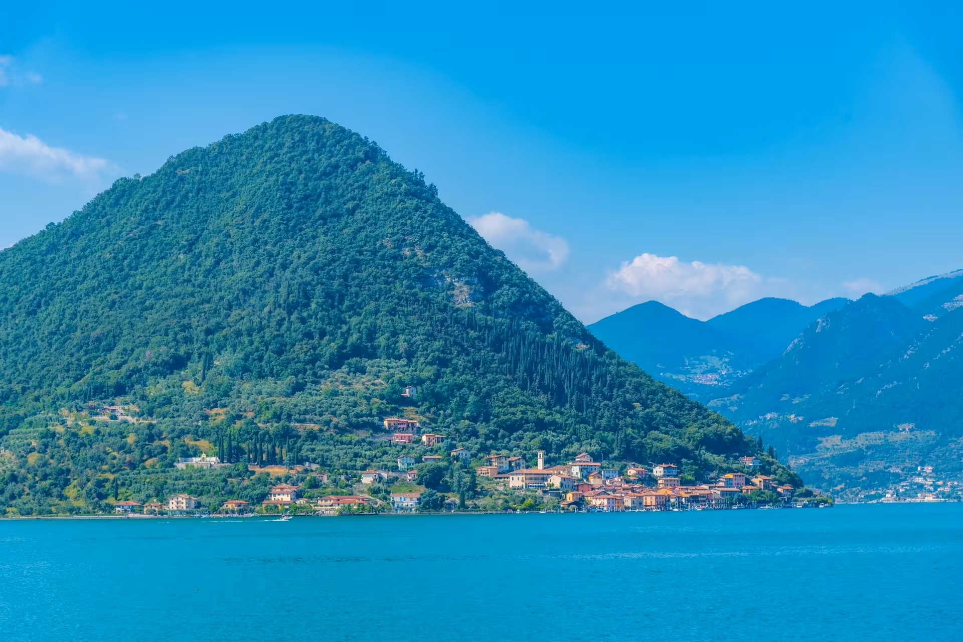 Picturesque island in Lake Iseo surrounded by emerald waters and green hills, highlighting Franciacorta's natural beauty.