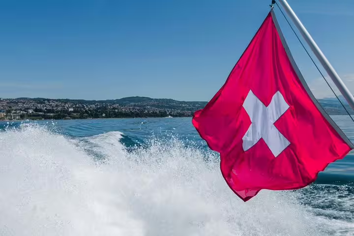 Swiss flag waves on a boat during a scenic Lake Lucerne cruise with Mount Rigi in the background.
