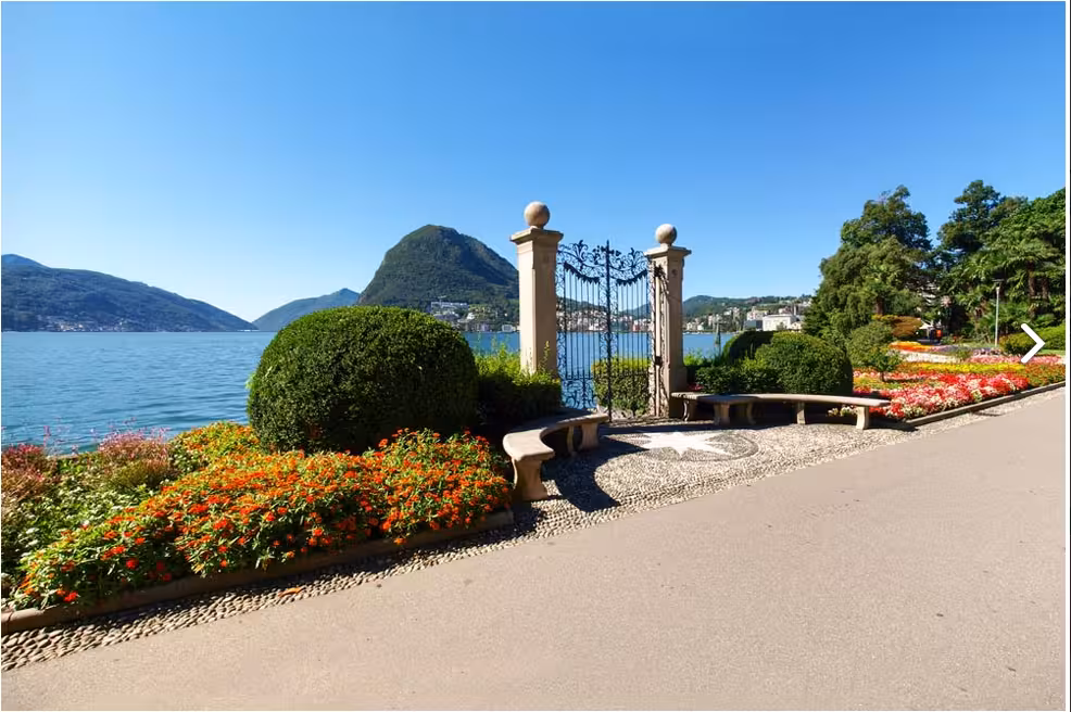 Picturesque Lake Lugano view with vibrant flower gardens and historic gate, ideal for a day trip from Milan.
