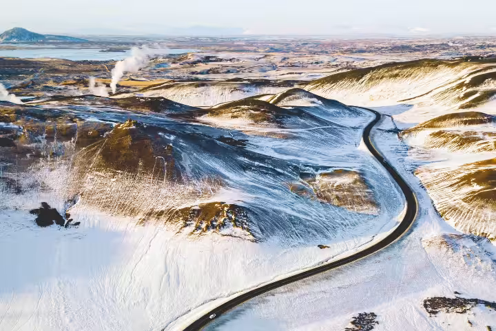 Aerial view of a winding road through snow-covered volcanic hills near Lake Myvatn, Iceland