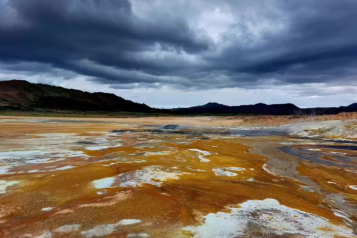 Colorful geothermal hot springs with orange mineral deposits under dramatic stormy sky at Lake Myvatn, Iceland