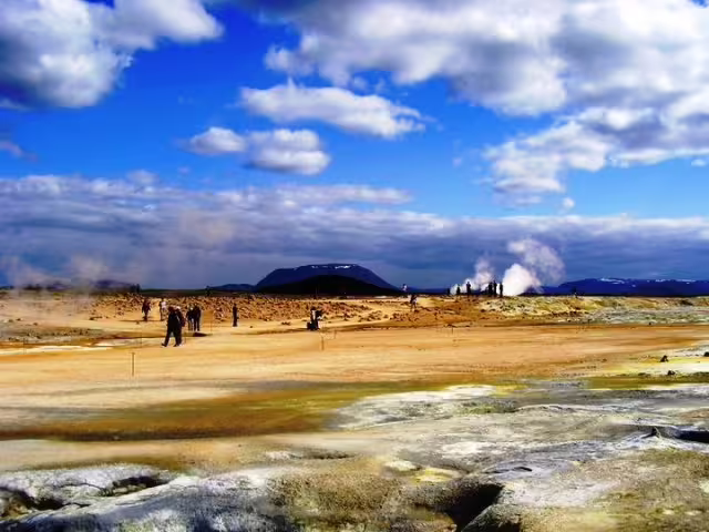 Geothermal landscape at Lake Myvatn Iceland with steam vents, tourists, volcanic mountains and blue sky