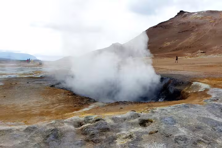 Steaming geothermal mud pool at Lake Myvatn with volcanic landscape and visitors in background
