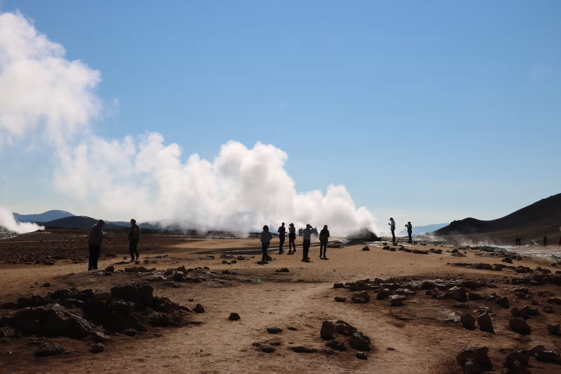 Tourists silhouetted against steaming geysers at Lake Myvatn geothermal area in Iceland under blue sky