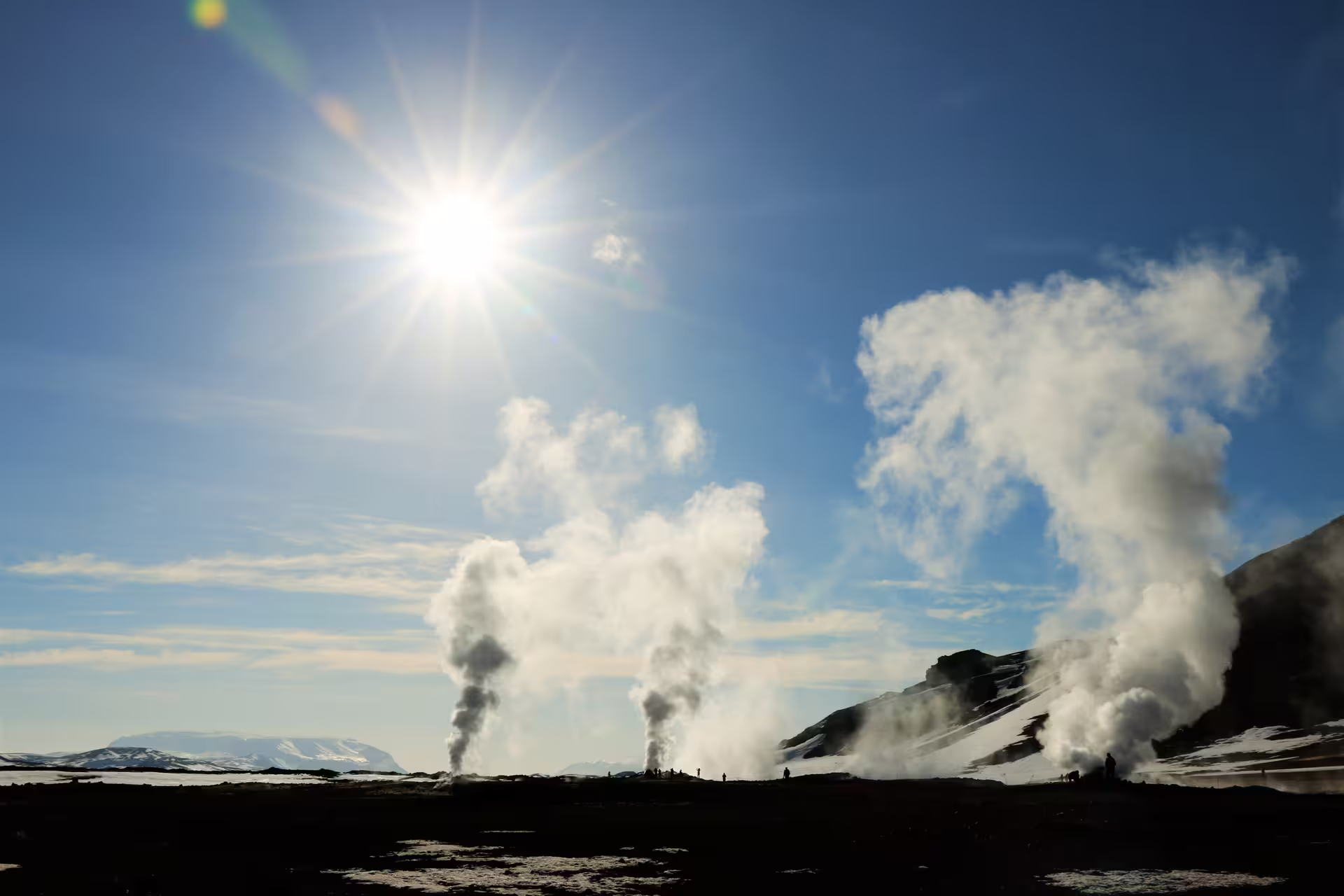Geothermal steam vents rising near Lake Myvatn Iceland under bright sun with snow-capped mountains
