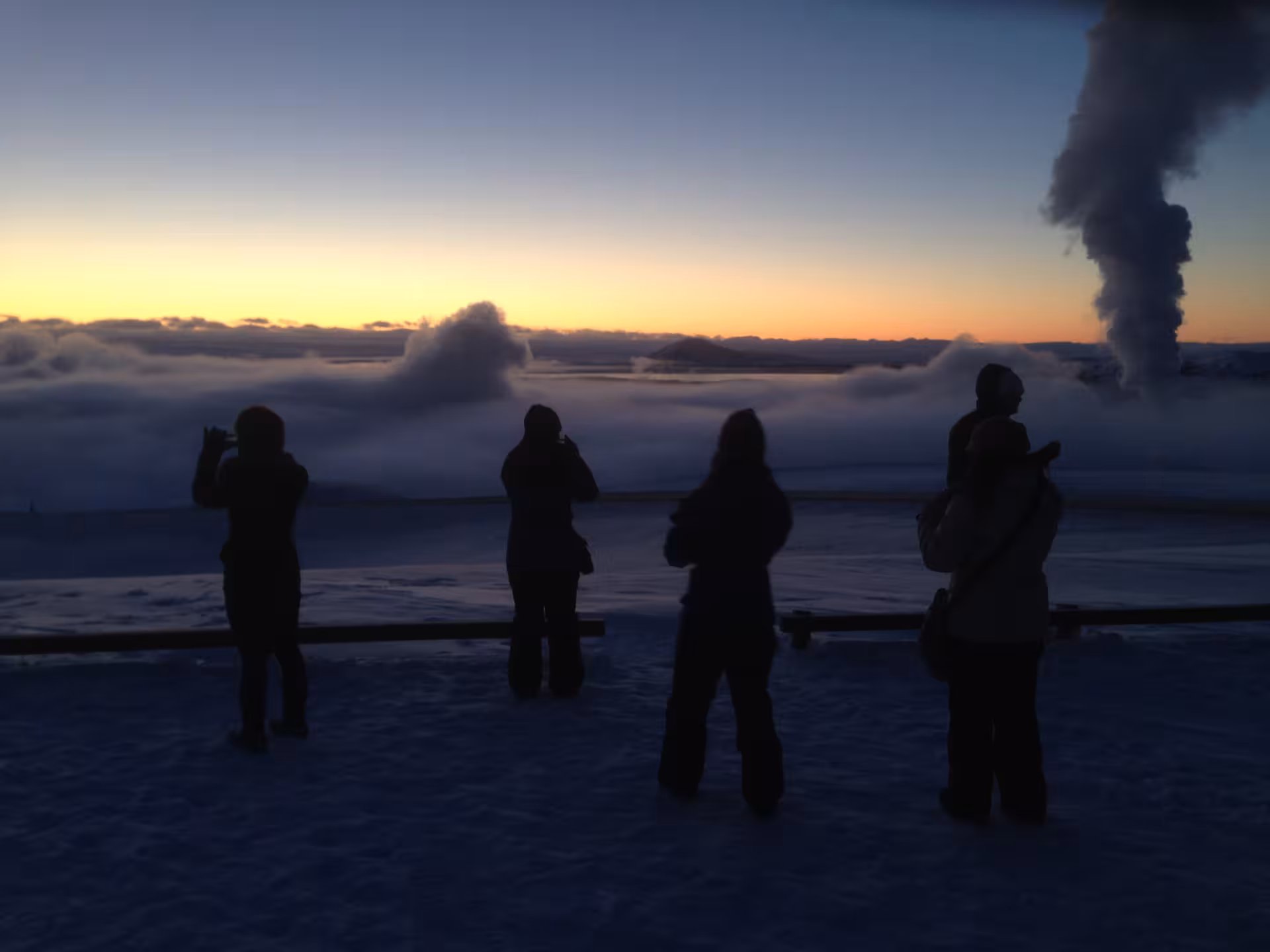 Tourists silhouetted at sunset watching geothermal steam rise over snowy Lake Myvatn on a guided Iceland day tour