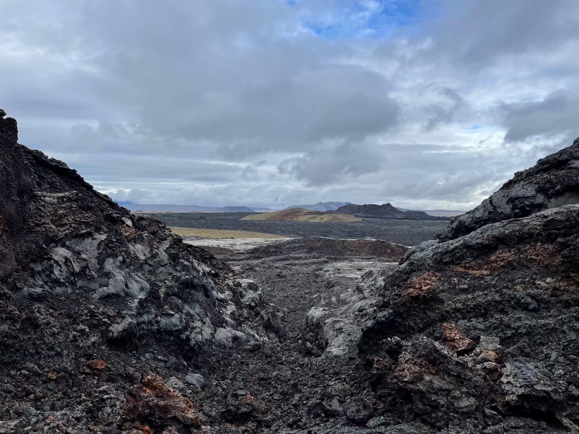 Rugged black lava field with volcanic craters and mountains under cloudy sky near Lake Myvatn, Iceland