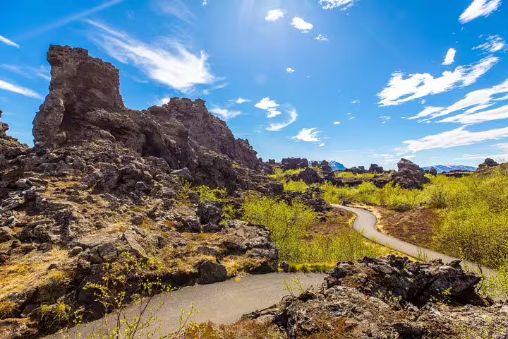 Rugged lava rock formations with winding path through green shrubs at Lake Myvatn, Iceland under blue sky