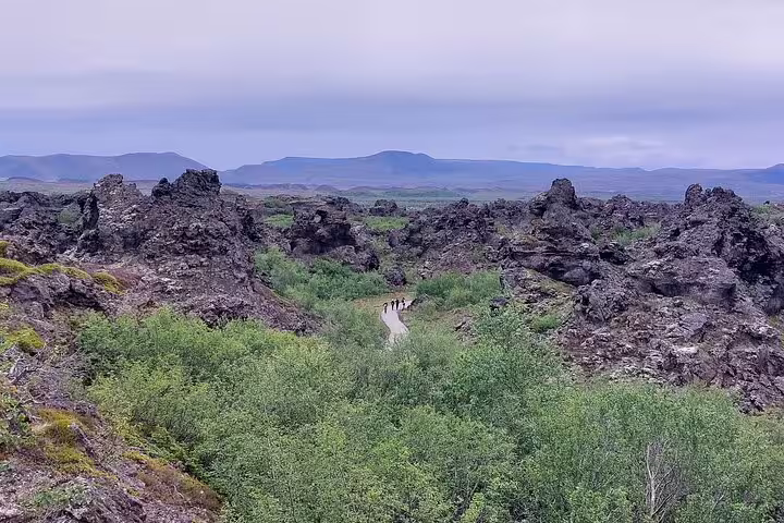 Hikers walking a narrow path through Dimmuborgir lava rock formations near Lake Myvatn, Iceland
