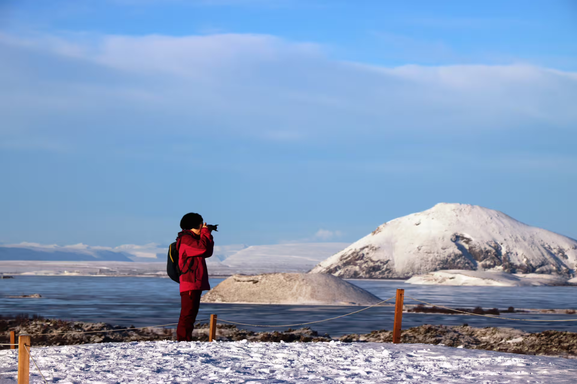 Photographer in red jacket capturing snowy Lake Myvatn pseudo craters and mountains in winter Iceland
