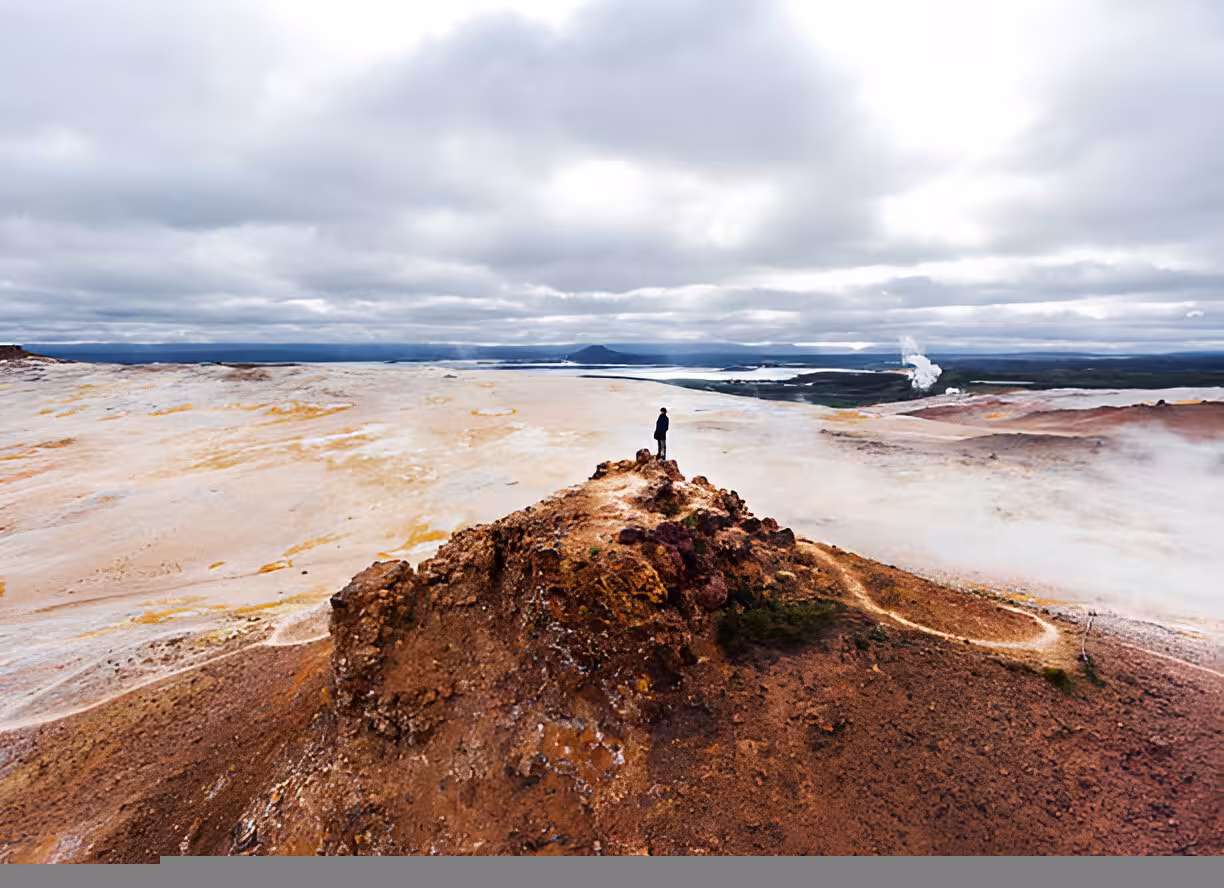 Person standing on volcanic ridge overlooking geothermal landscape near Lake Myvatn, Iceland