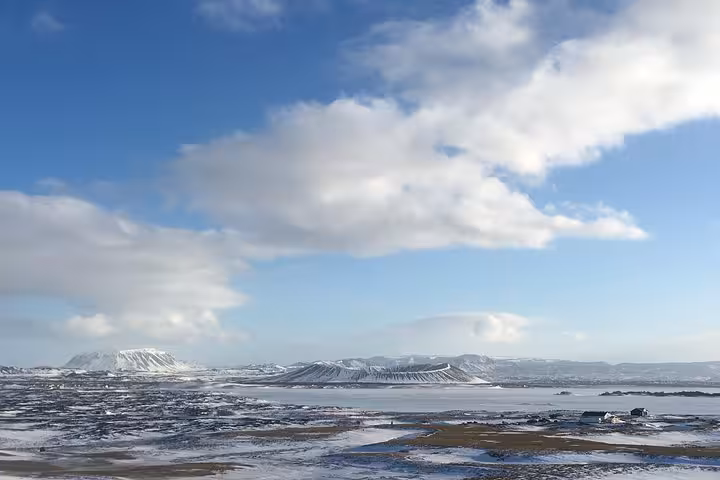 Panoramic winter view of Lake Myvatn's snow-covered landscape under a blue sky with scattered clouds.