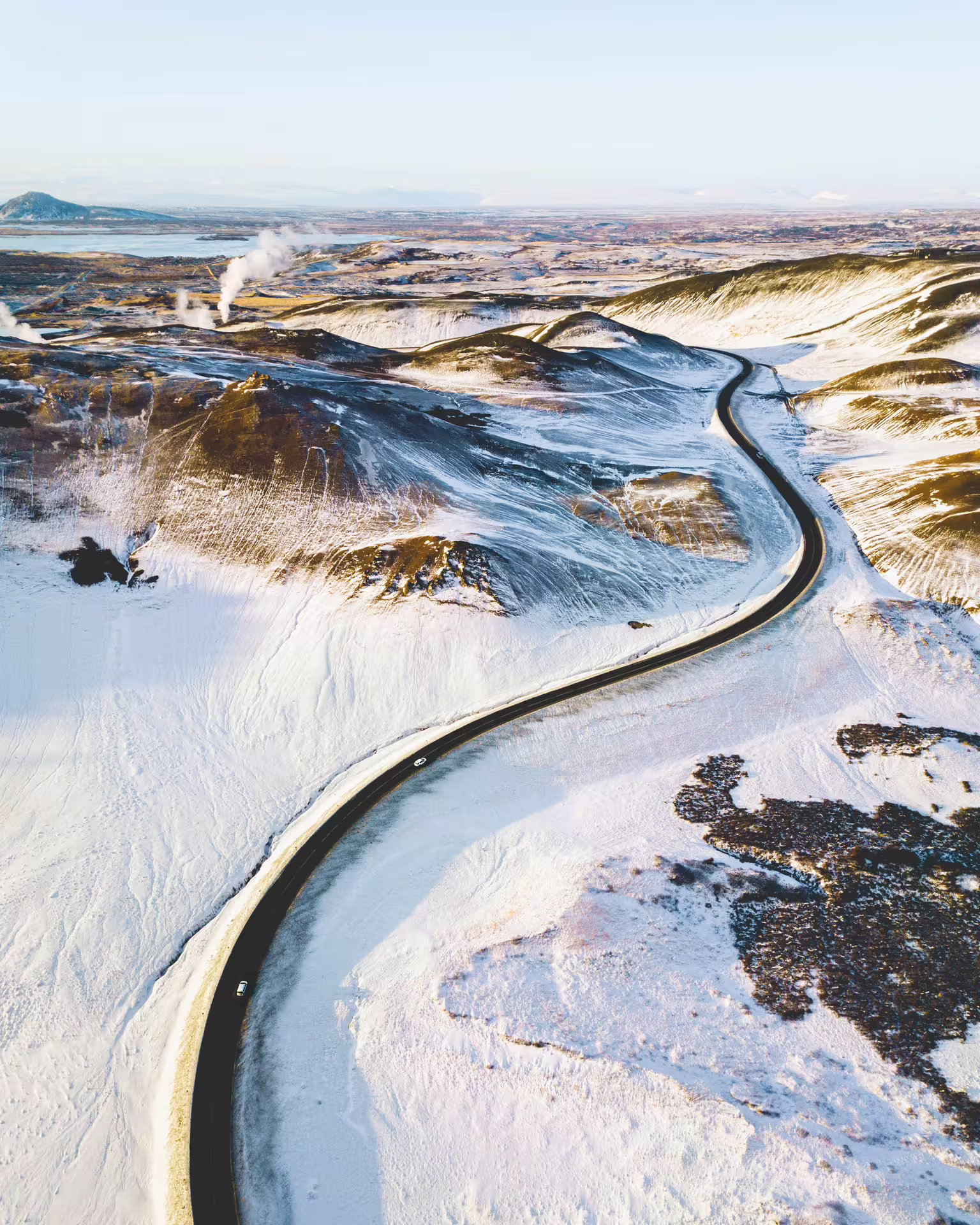 Aerial view of a winding road through snow-covered volcanic hills near Lake Myvatn, Iceland in winter