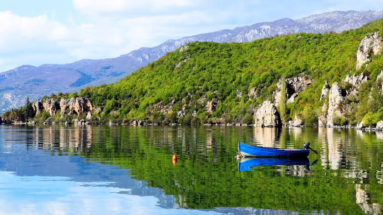 Discover the serene vistas of Lake Ohrid with a calm blue boat reflecting the lush greenery on a Macedonia day trip.