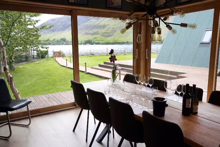 Cozy lakeside wine tasting venue with wine glasses and bottles on a wooden table with scenic mountain views.