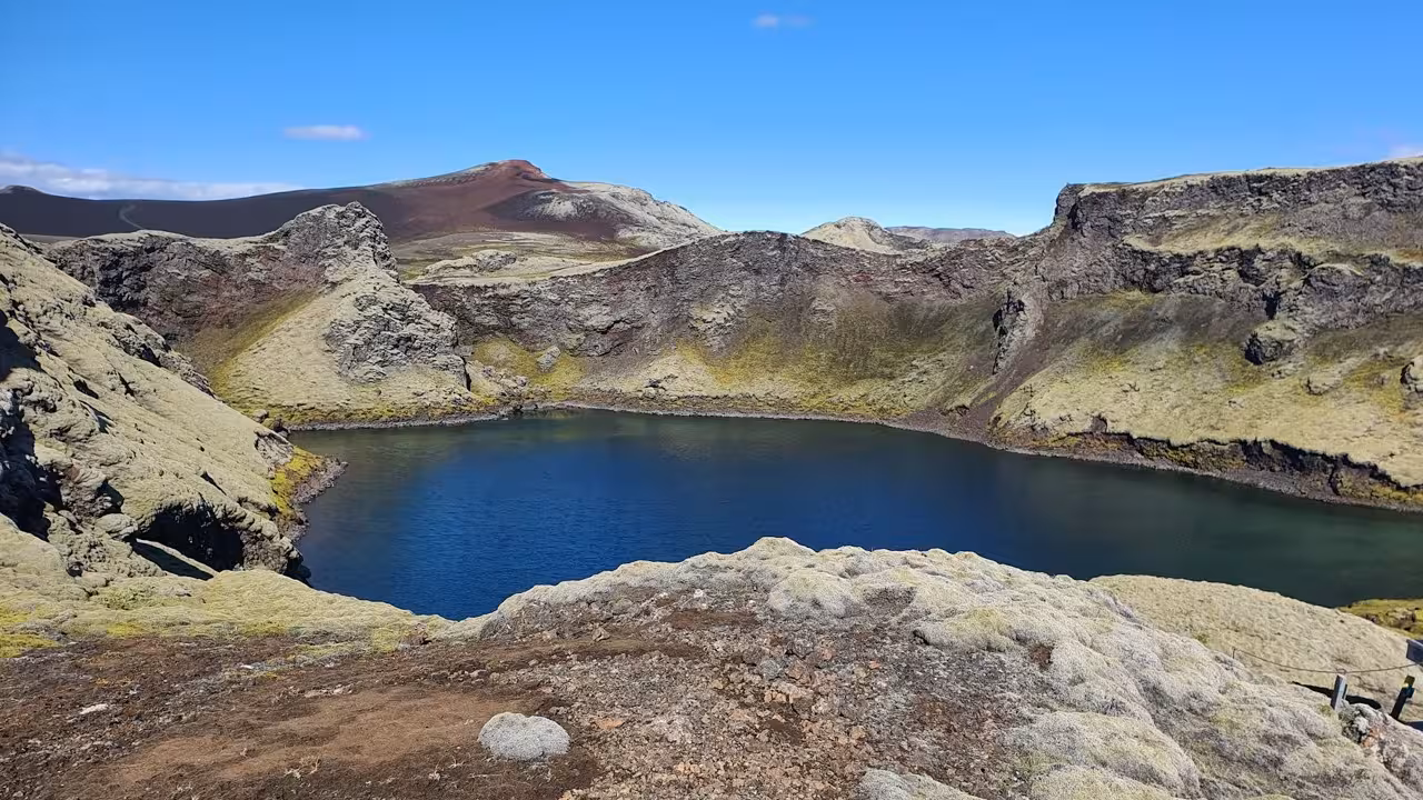 Blue crater lake surrounded by moss-covered lava rocks and volcanic mountains at Laki, Iceland