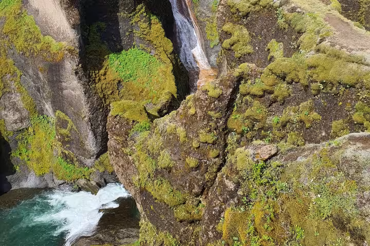 Moss-covered volcanic canyon walls with turquoise river and waterfall in South Iceland