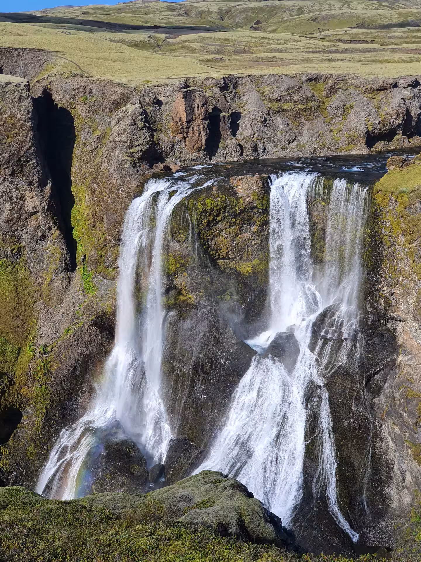 Cascading waterfall with rainbow mist over mossy volcanic rocks near Laki, South Iceland