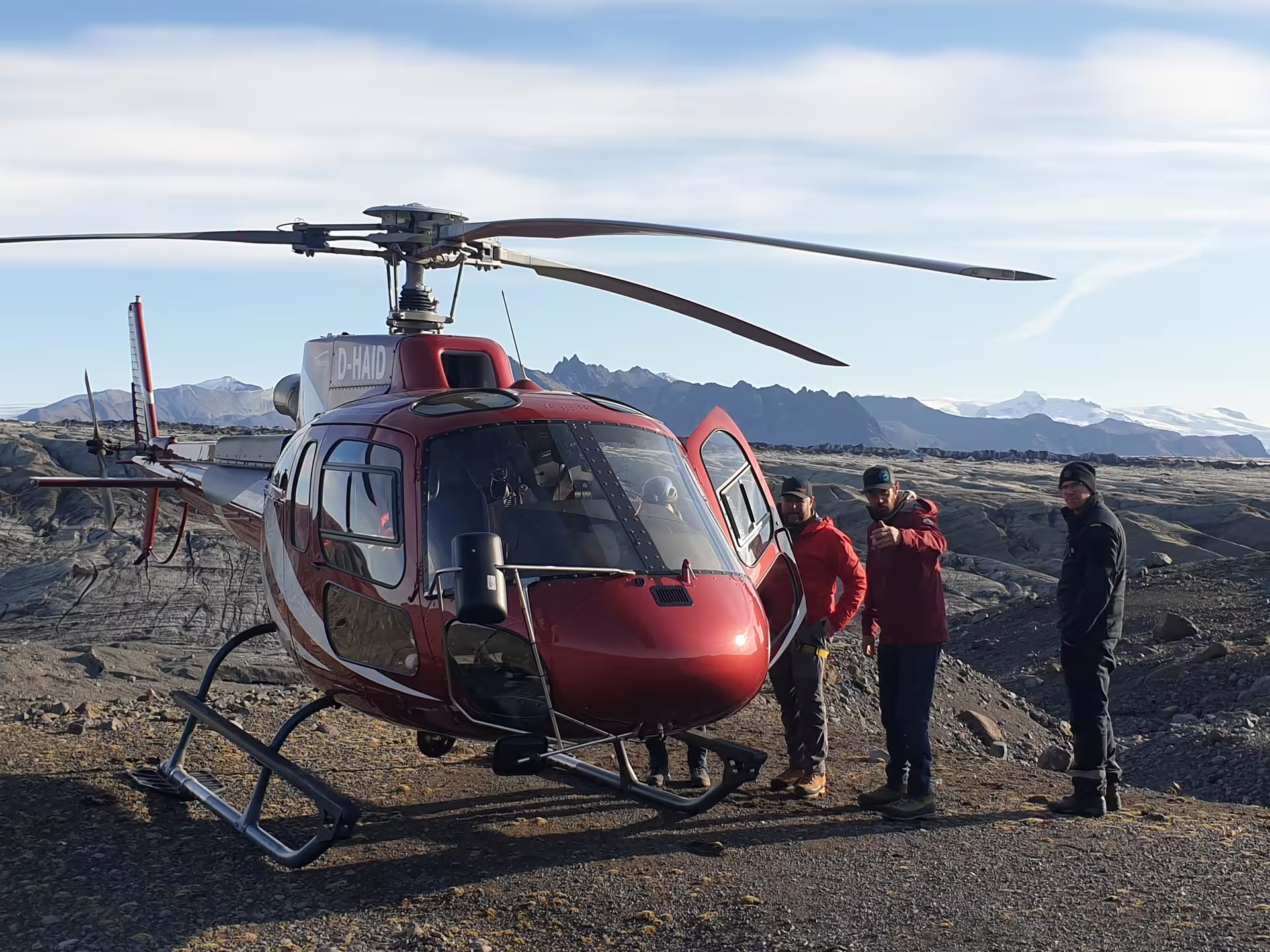 Red helicopter D-HAID landed on volcanic terrain near Skaftafell with three people standing beside it