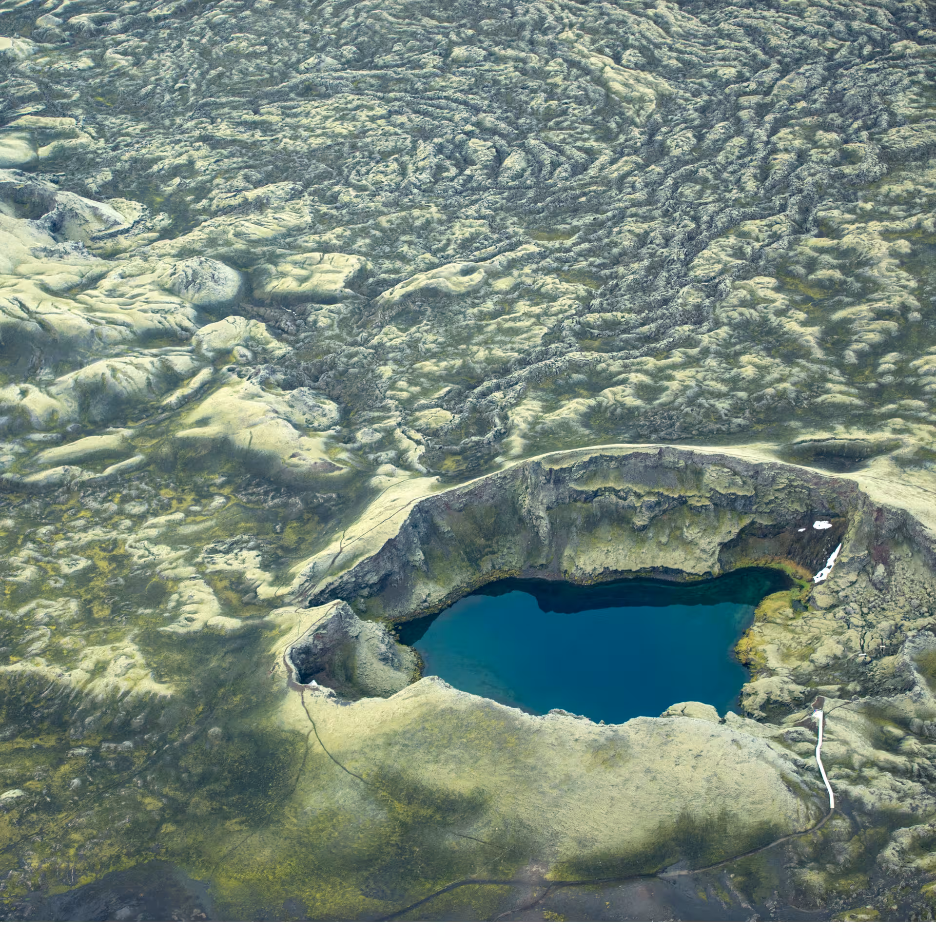 Aerial view of a turquoise crater lake surrounded by ancient moss-covered lava fields on Laki Craters super jeep tour from Vik Iceland