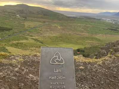 Summit marker sign for Lali at 242m elevation overlooking green Iceland lava field valley