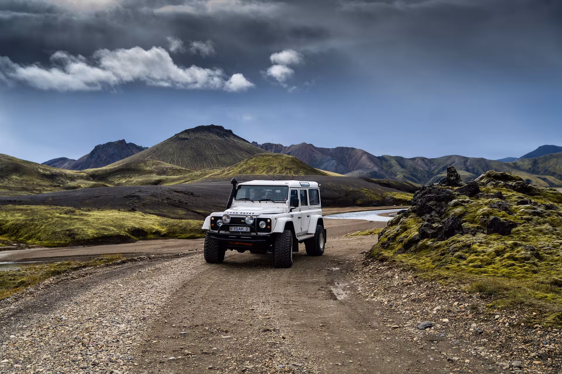 White Land Rover Defender on gravel road in Iceland's colorful highland mountains under dramatic sky