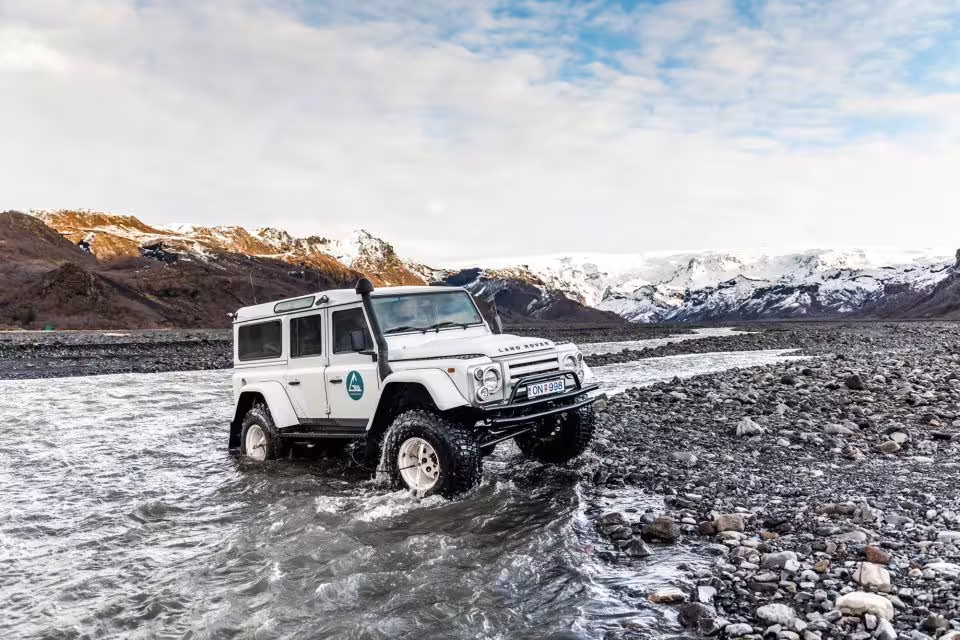 White Land Rover Defender fording a glacial river in Thorsmork with snow-capped volcanoes behind